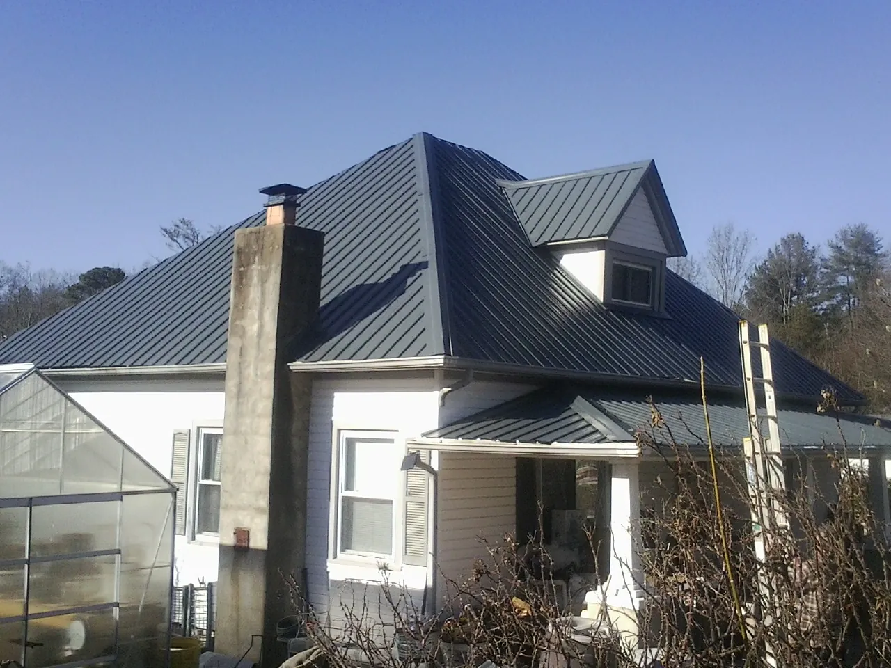 Dark blue standing seam metal roof on a white farmhouse with dormer — Slate & Tile Roof Repair by Roofing Brothers in Helena