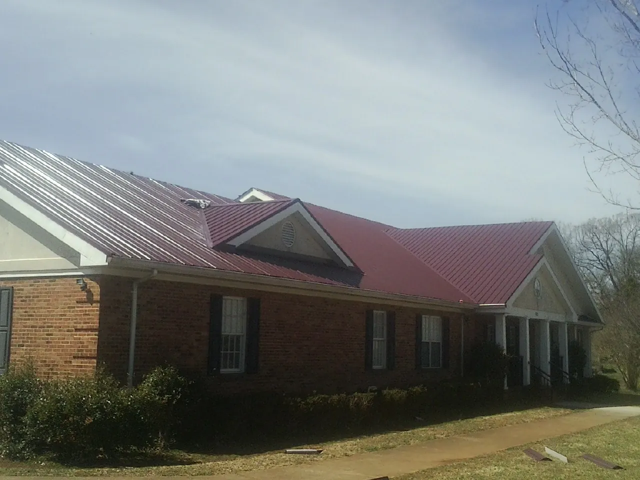 Red metal roof with gabled entries on a long brick building, from a Hail Damage Roof Repair job in Helena