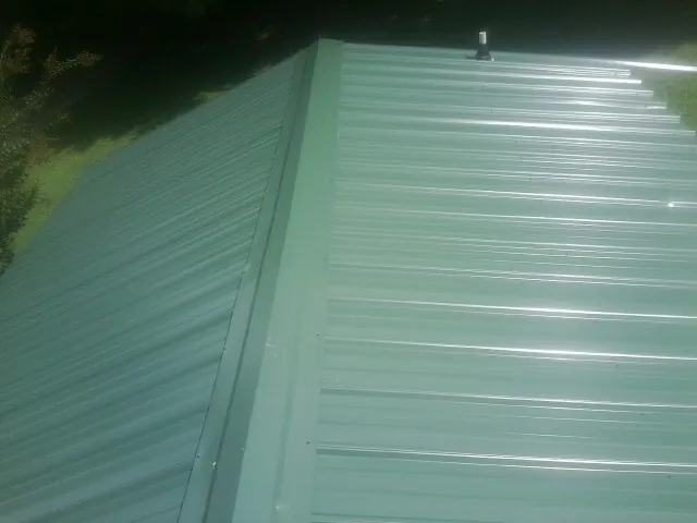 New green metal panels meeting at the ridge of a roof — Flat Roof Repair work by our crew in Helena